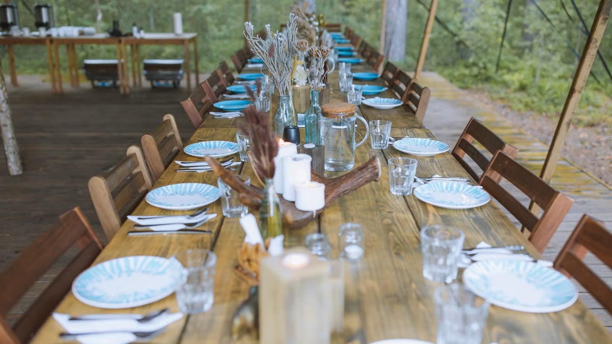 A beautifully set rustic wooden table under a tent, creating a charming outdoor dining experience.